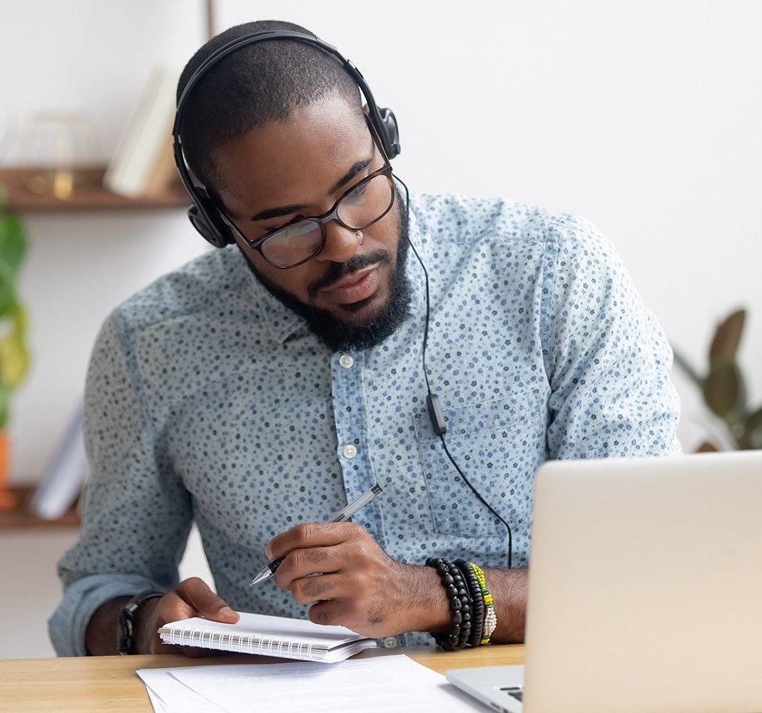 Focused,African,Business,Man,In,Headphones,Writing,Notes,In,Notebook