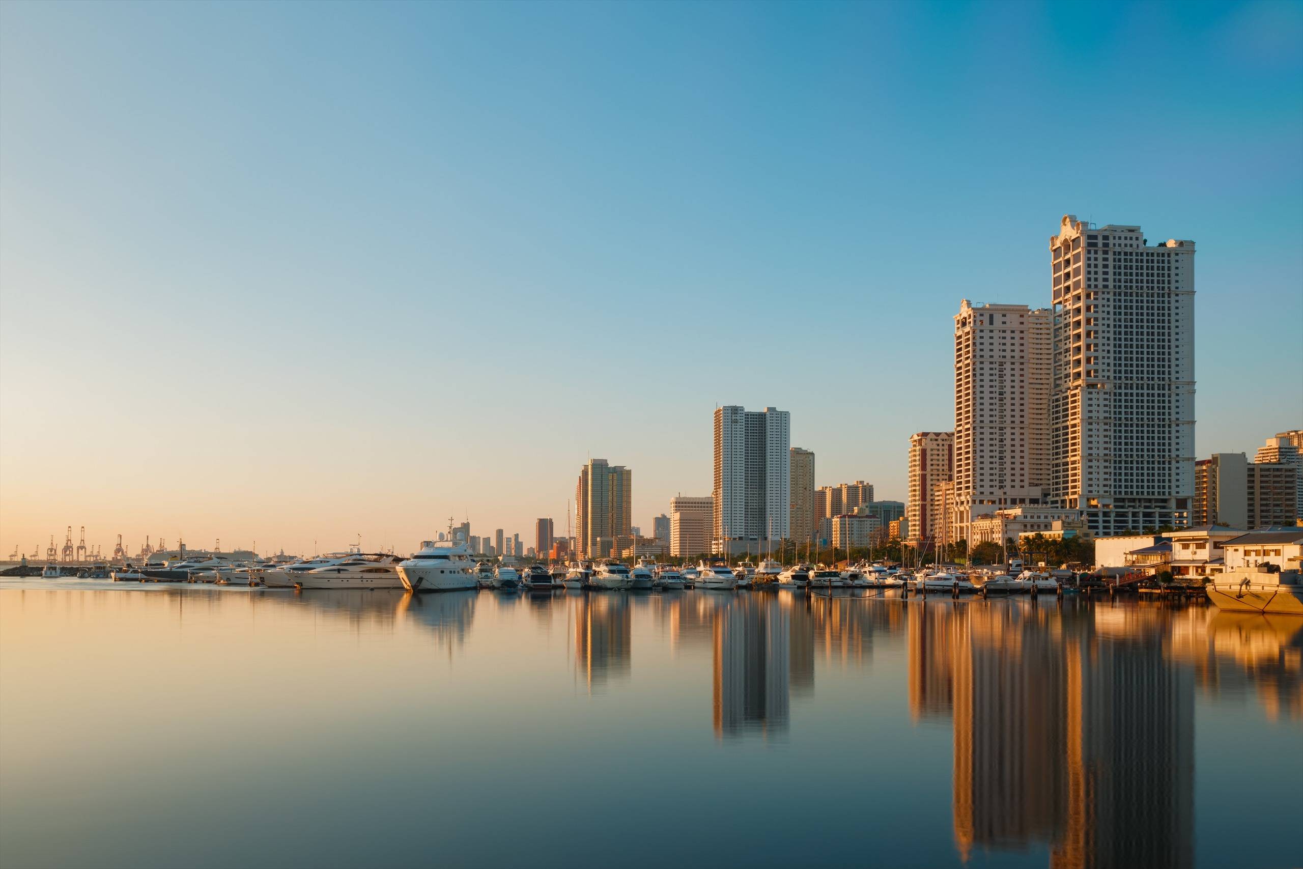 Manila skyline and marina reflected in calm water at sunset.
